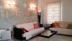 A living room with a stone wall, two sofas, a glass coffee table, and a lamp. - Villa Koumneni - Sea and mountain peace and tranquility (Paphos)