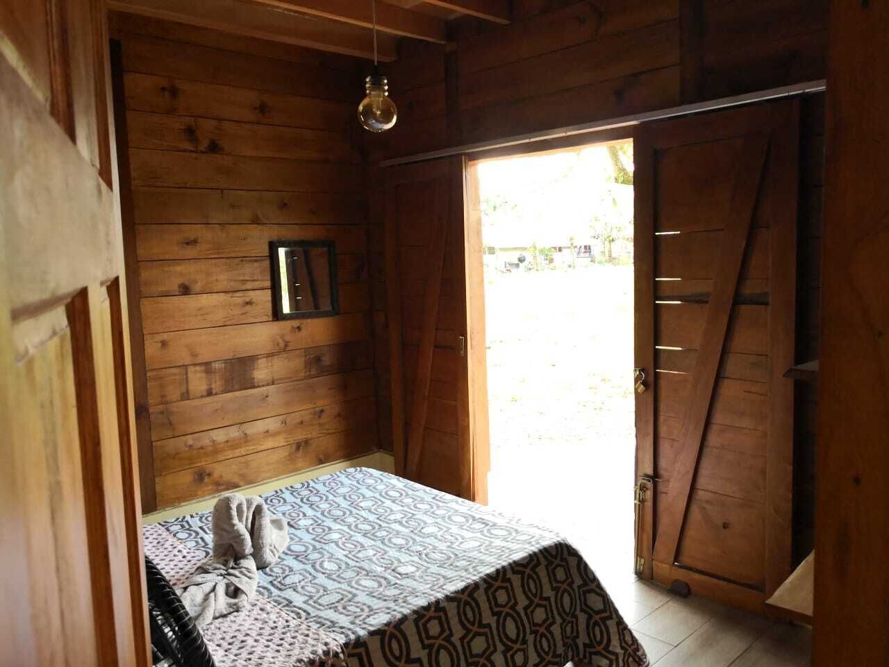 Ein Zimmer in einer Holzhütte mit einem Bett, einer Hängeleuchte und einer Tür, die nach draußen führt.