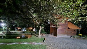 Uma cabana rústica de madeira com um pequeno lago e um caminho pavimentado que leva até ele.