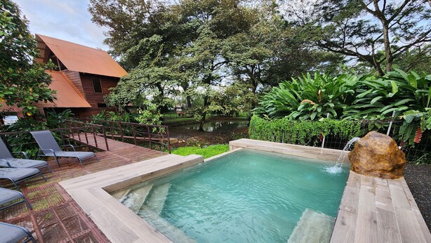 Piscina retangular com deck de madeira e cadeiras de metal.
