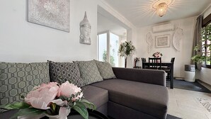A modern living room with a sofa, a vase with flowers, and a dining area with a table and chairs. - AP290 - Casa Olivia (Nerja)