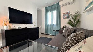 A modern living room with a flat-screen TV, a sofa, a coffee table, and a potted plant. - AP290 - Casa Olivia (Nerja)