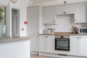 Une cuisine moderne avec des meubles blancs, un four encastré, un four à micro-ondes et un grille-pain.