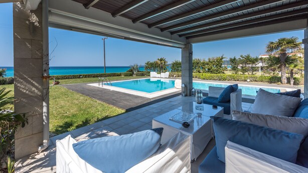 A covered outdoor area with a pool, white furniture, and a view of the sea.