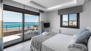 A bedroom with a large bed, a TV, and a balcony with a view of the sea.