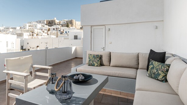 Eine Dachterrasse mit einer Sitzecke, Sofas, Stühlen und einem Tisch mit dekorativer Schale und Kerzen.