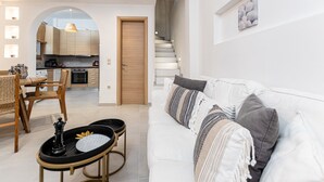 Ein modernes Wohnzimmer mit einem weißen Sofa, einem Essbereich mit Holztisch und -stühlen, einer durch einen Bogen sichtbaren Küche und einer Treppe, die zu einer anderen Etage führt.