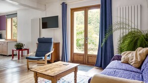 A modern living room with a sofa, a wooden coffee table, a blue armchair, and a TV mounted on the wall.