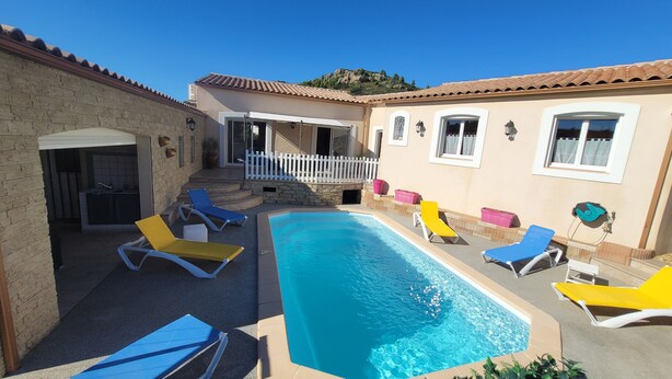A swimming pool with lounge chairs, a stone wall, and a building with a tiled roof.