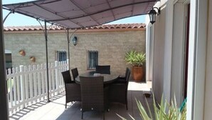 An outdoor patio with a round table and chairs, a potted plant, and a white fence.