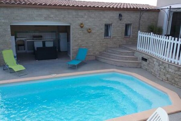 A stone building with a swimming pool, outdoor seating, and a fenced area.