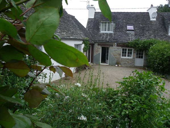 A stone house with a gravel driveway and a garden with various plants and flowers.