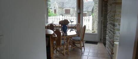 A dining area with a table and chairs, a view of the outside, and a stone wall.