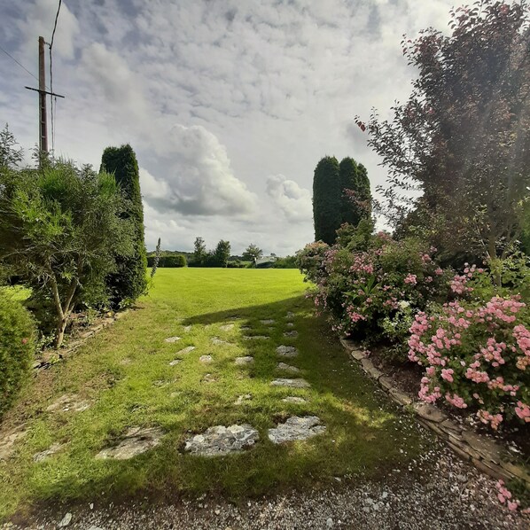 A grassy pathway with stepping stones leading through a garden with pink flowers and trees. - Charming house in Locquirec (Locquirec)