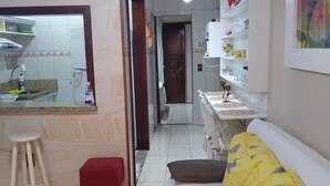Una cocina con un lavamanos, taburetes y una encimera. Hay un pasillo que conduce a un dormitorio con una cama y un sofá.