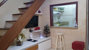 Una escalera con escalones de madera, un mueble blanco para entretenimiento con un televisor, un pequeño árbol de Navidad y un taburete rojo.