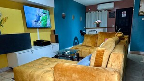 Ein Wohnzimmer mit einer Couch, einem Fernseher, einem kleinen Tisch und einem Schrank.