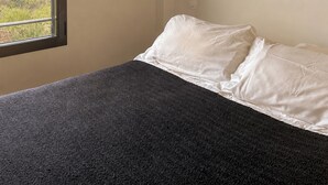 Ein Schlafzimmer mit Bett, Fenster mit Blick, Wandleuchte und einer gewebten Wanddekoration.