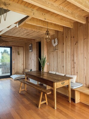 A wooden interior with a long table, benches, and a hanging light fixture.