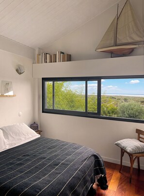 Ein Schlafzimmer mit einem großen Fenster, einem Bett, einem Sessel und einem Modell eines Segelboots.