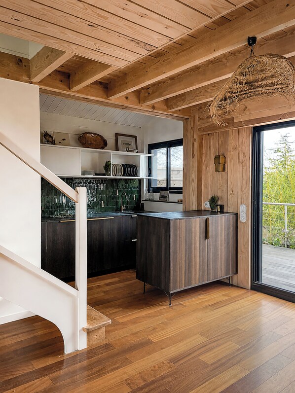 A modern kitchen with wooden beams, a black countertop, and a hanging light fixture.