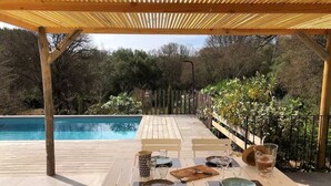 Un espace extérieur abrité où l’on peut prendre ses repas, avec une piscine en arrière-plan.