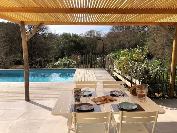 A covered outdoor dining area with a pool in the background. - House Porto Vecchio 8 pers. with pool can be heatable  (Porto-Vecchio)