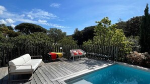 Une terrasse en bois avec une piscine, un canapé blanc et une chaise rouge.