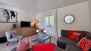 Un salon comprenant un canapé, un fauteuil, une table basse, un téléviseur et des œuvres d’art accrochées au mur.