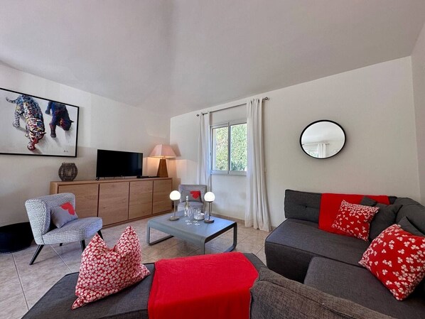 A living room with a sofa, armchair, coffee table, TV, and artwork on the wall.