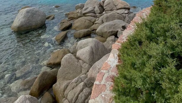 Un paysage côtier caractérisé par une eau claire, une côte rocheuse et des collines à l’horizon.