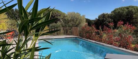 A rectangular swimming pool with a wooden deck and a lounge chair.