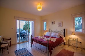 A bedroom with a bed, a desk, and a chair. There is a sliding glass door leading to an outdoor area with chairs and a table. - Maritsa Villa (Neo Chorio)
