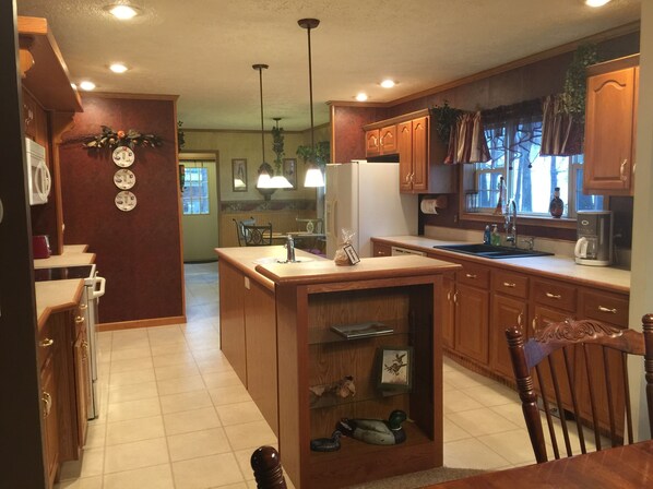 A kitchen with wooden cabinets, a central island, pendant lights, and a view of the dining area. - Duck Hunting, Fishing or Relaxing Family Vacation (Hornbeak)