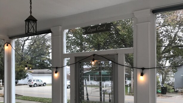 En overdækket veranda med store vinduer, en dør og lyskæder.