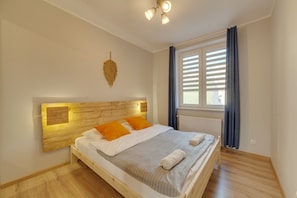A neatly made bed with white and orange bedding, a wooden headboard, and a window with blinds. - Dream Loft Krosna (Gdansk)