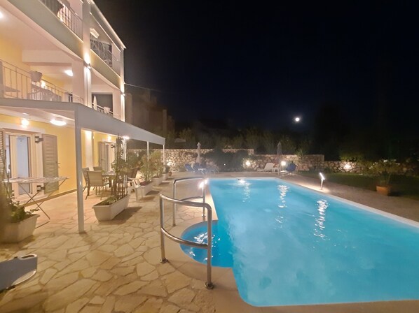 A swimming pool with a stone-tiled deck, surrounded by potted plants and outdoor furniture.