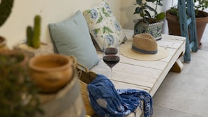 A wooden table with a wine glass and a straw hat, surrounded by potted plants and a woven basket.