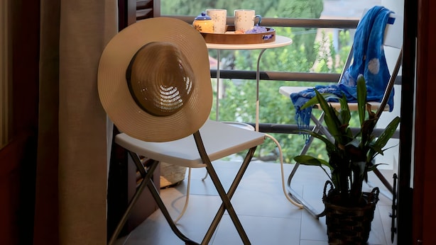 A balcony with a chair, a table with two cups, and a potted plant.