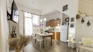 A compact kitchen with wooden cabinets, a dining table with chairs, a small side table, and a sofa.