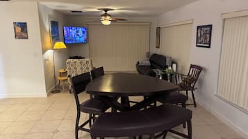 A dining area with a round table, chairs, a ceiling fan, a TV, and a lamp.