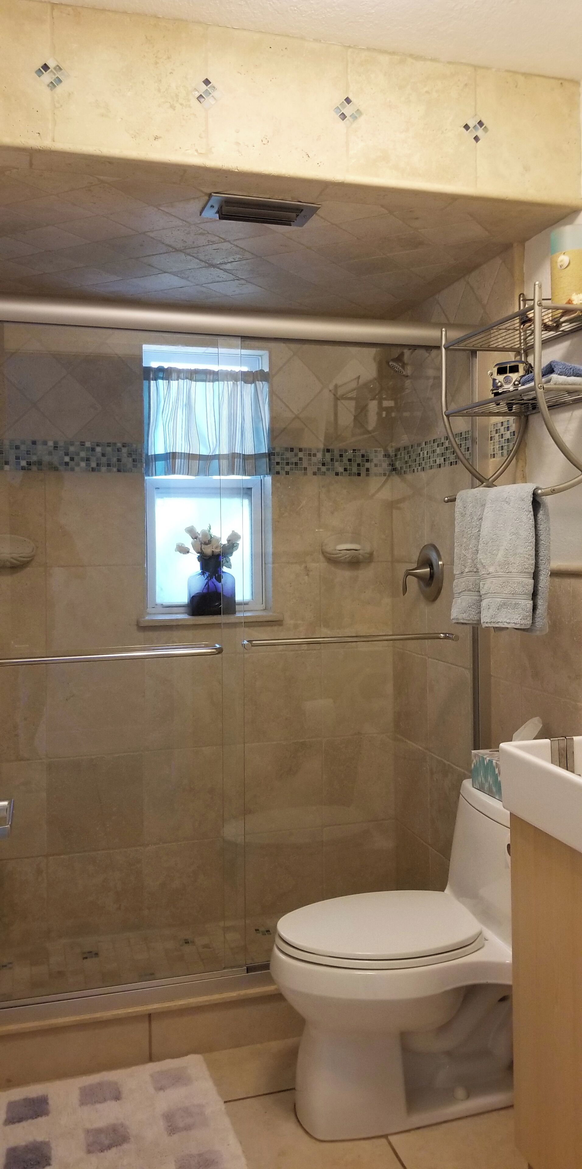Un baño con ducha de vidrio, inodoro y ventana con cortina.