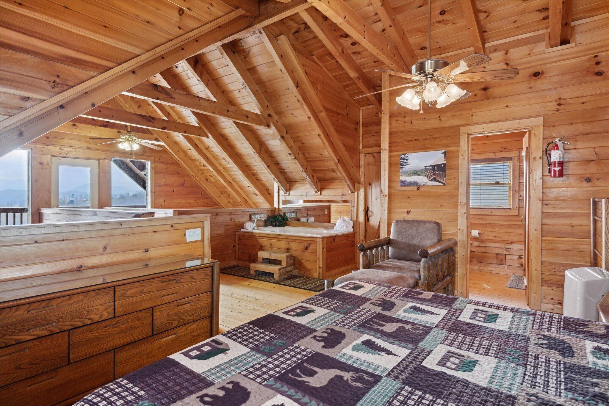 A cozy cabin with a wooden interior, a ceiling fan, a quilted bedspread, a wooden desk, and a chair.