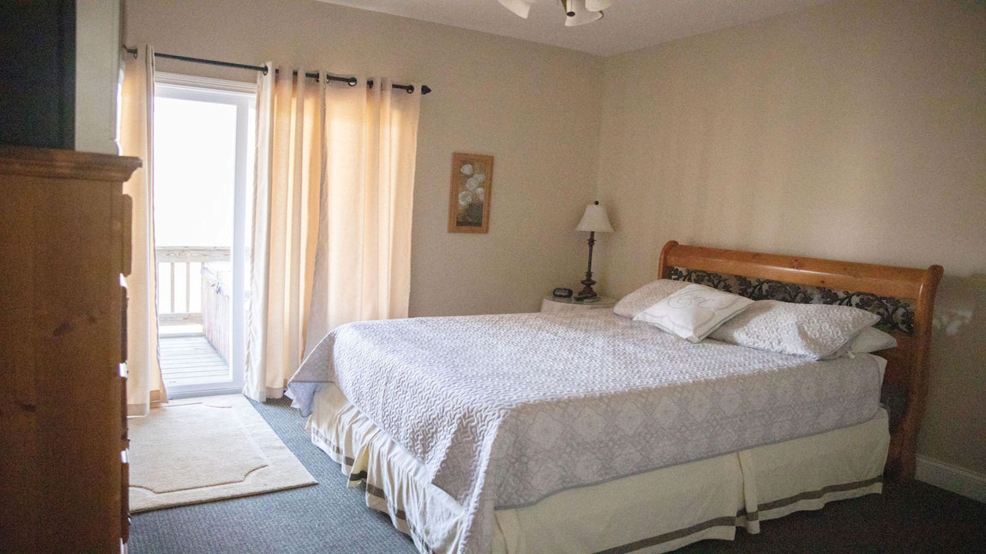 A bedroom with a large bed, a nightstand, a lamp, and a view of the outside.