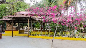 Ein überdachter Pavillon mit Ziegeldach, umgeben von leuchtend rosa blühenden Pflanzen und einer gelb gestrichenen Wand.