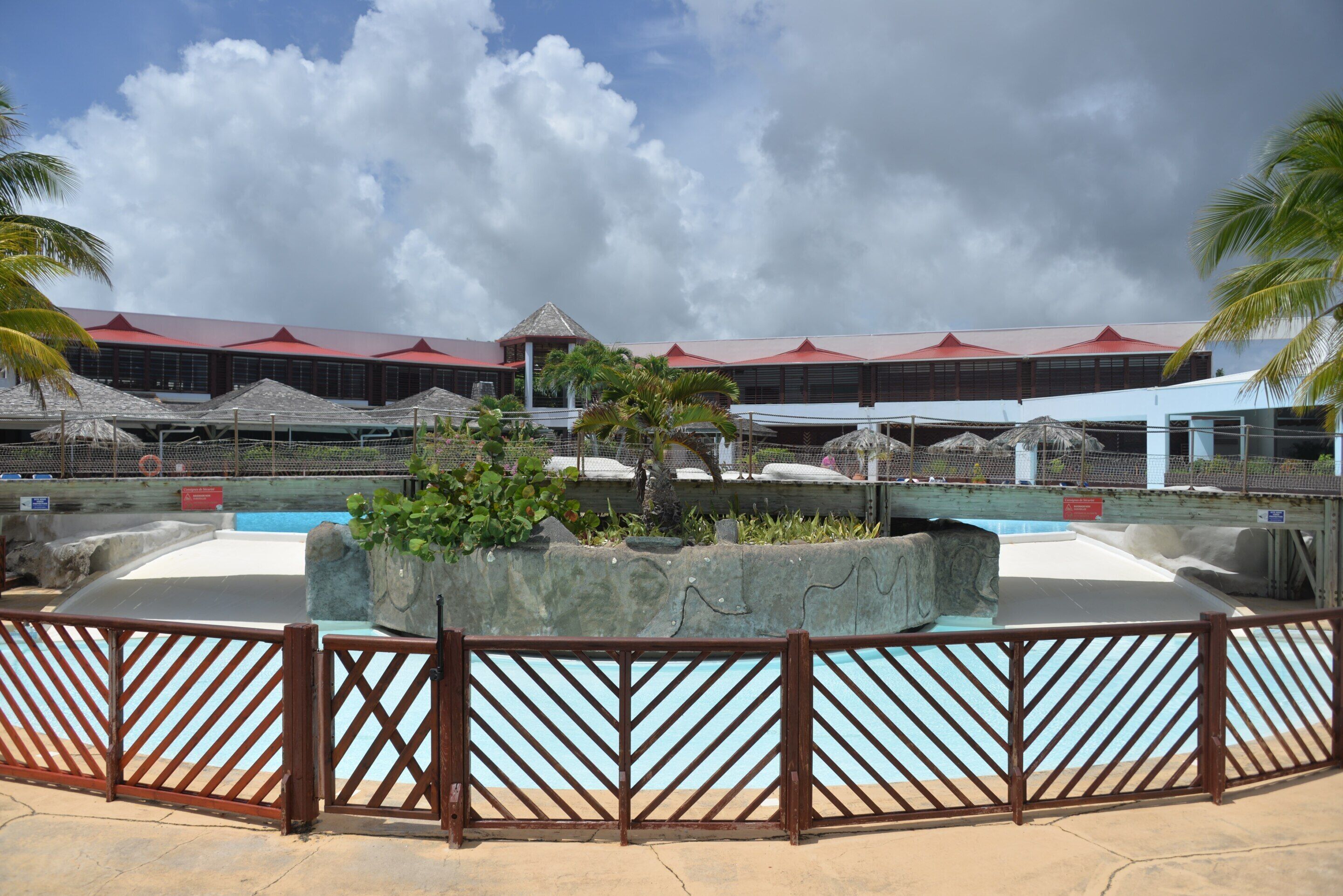 A resort with a pool area, palm trees, and a building with a red roof.