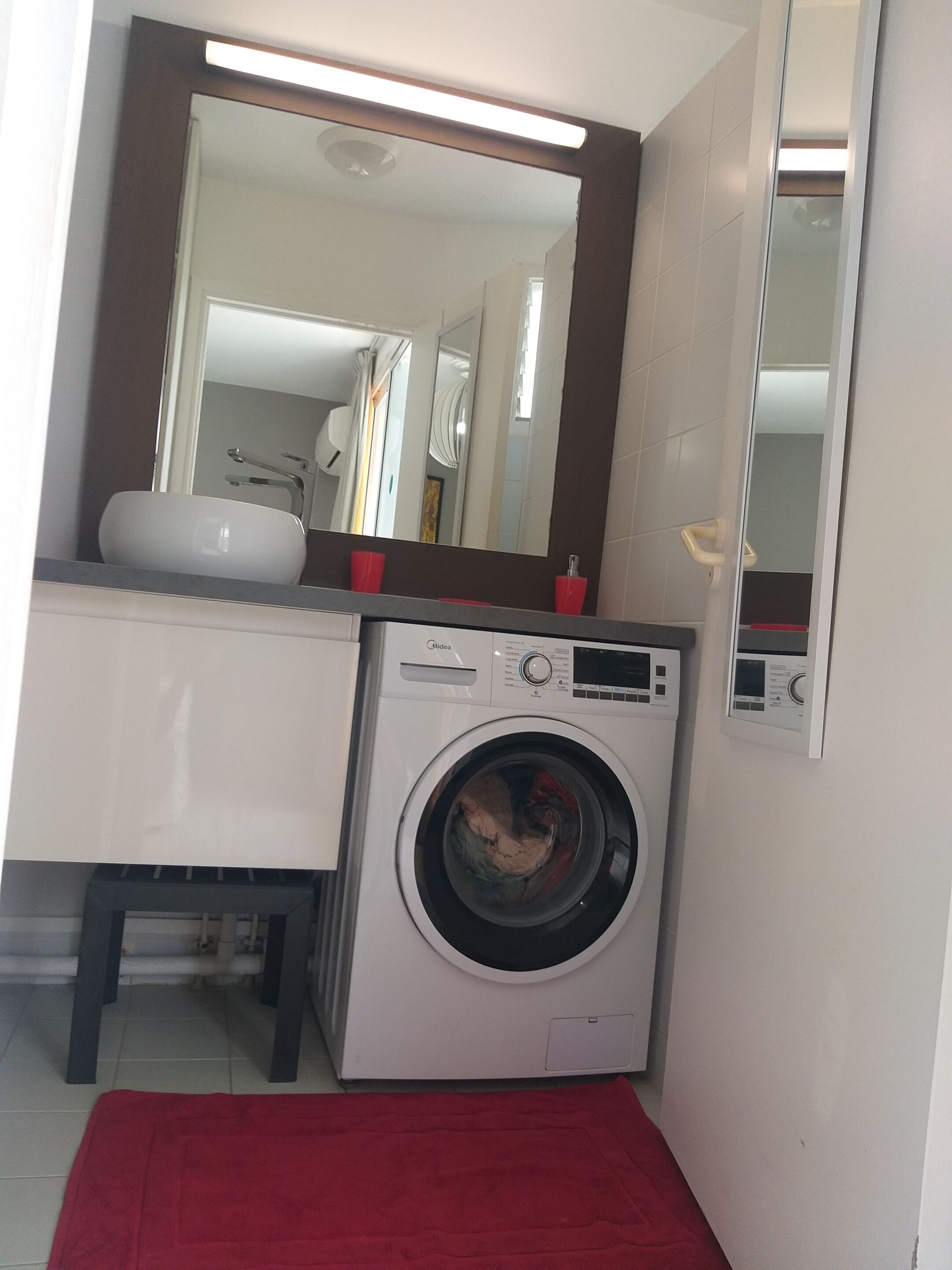 A compact bathroom with a washing machine, a sink, and a large mirror.