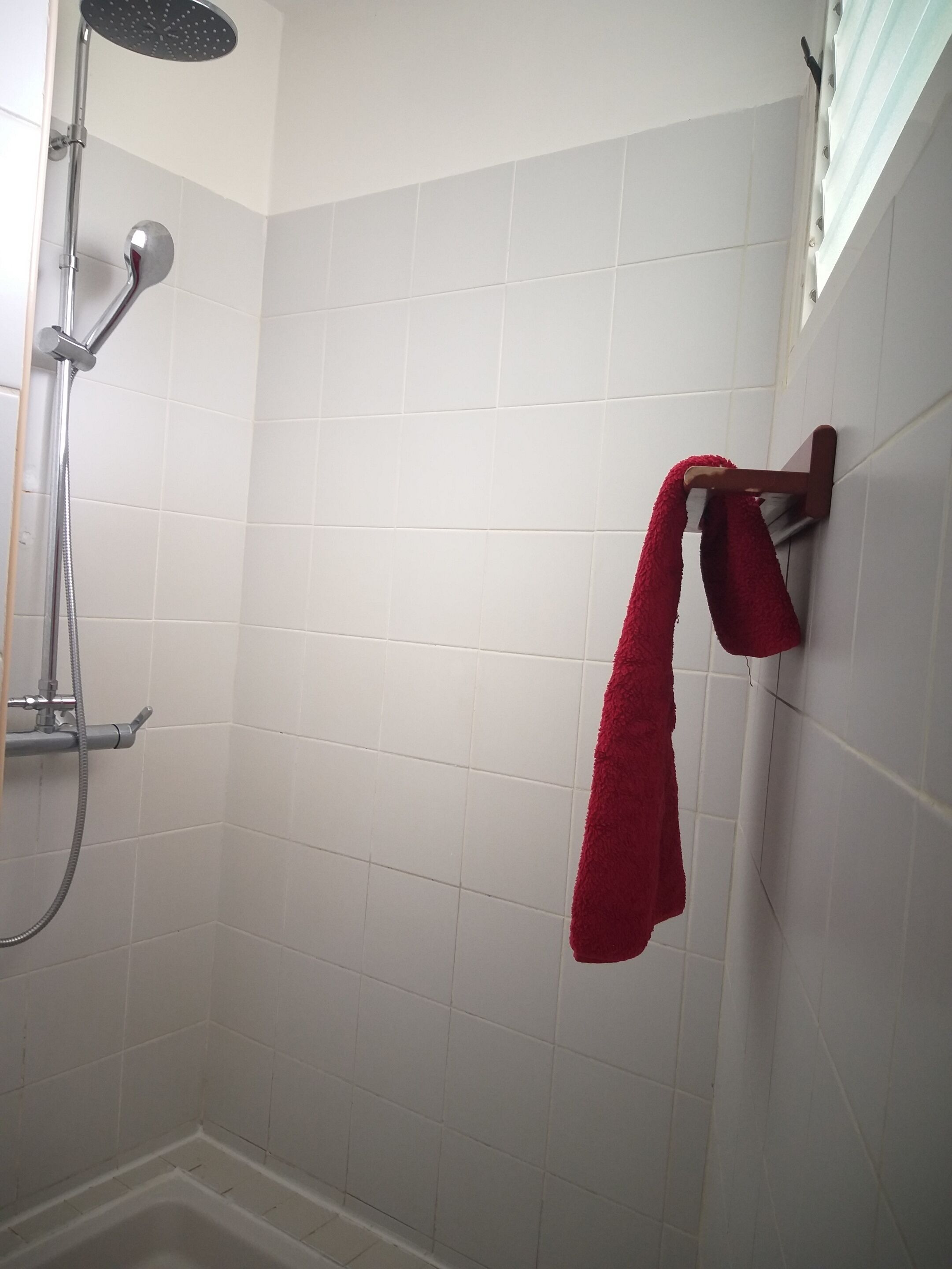 A shower area with white tiles, a handheld showerhead, and a red towel hanging on a wooden towel rack.