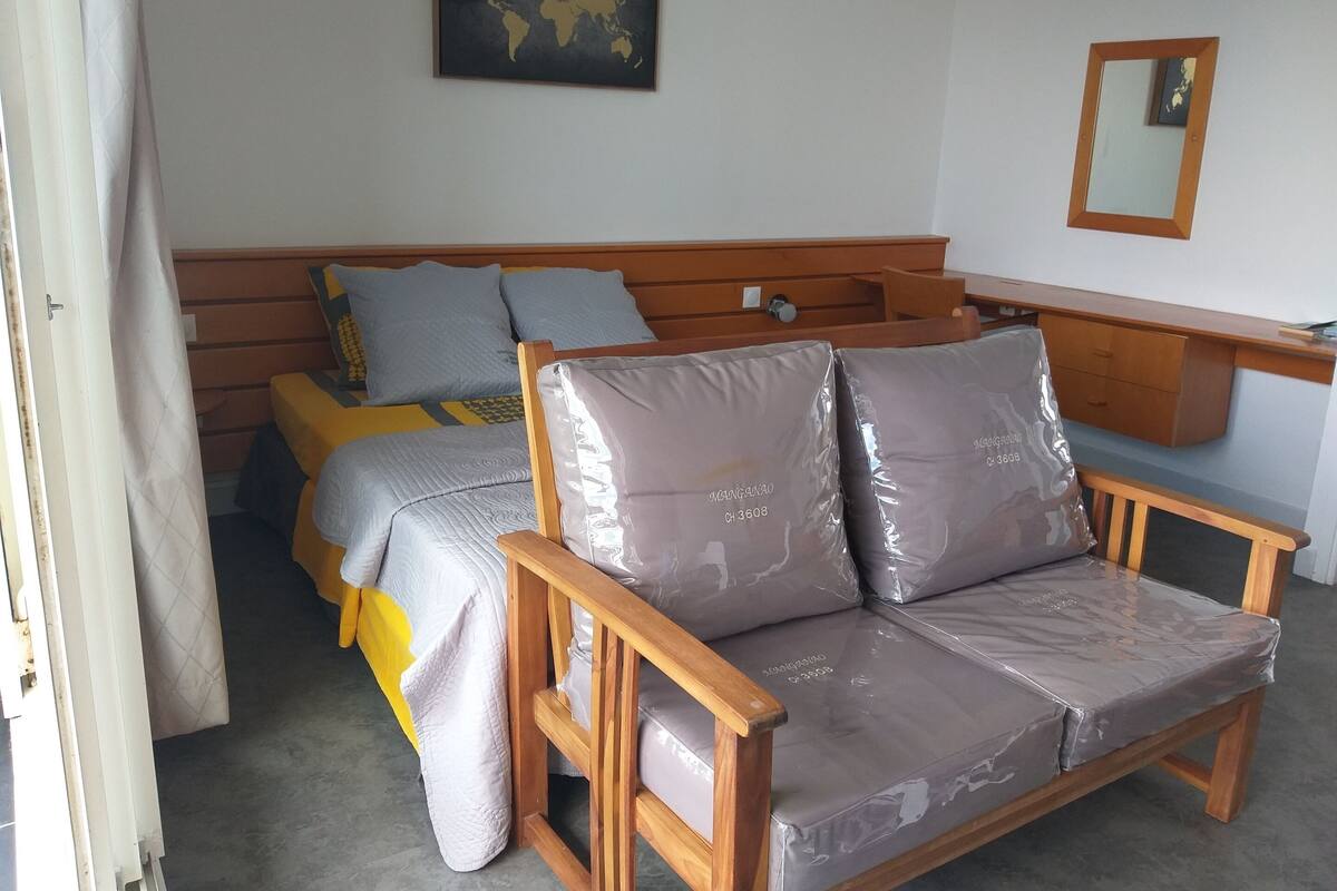 Une chambre à coucher avec un lit en bois, une chaise en bois, un petit bureau, une carte du monde accrochée au mur et un miroir.