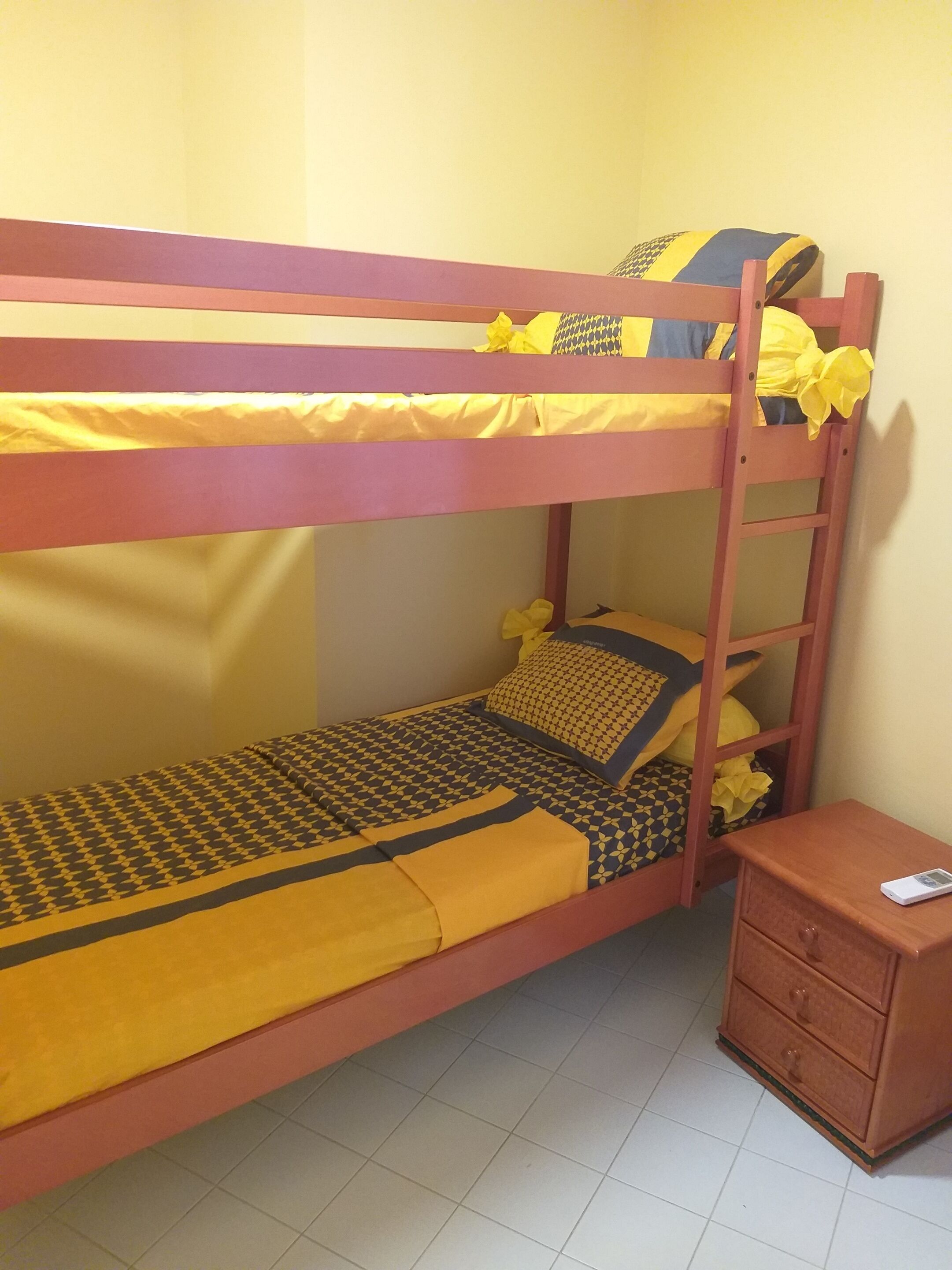 A bunk bed with yellow bedding and a wooden nightstand with drawers.